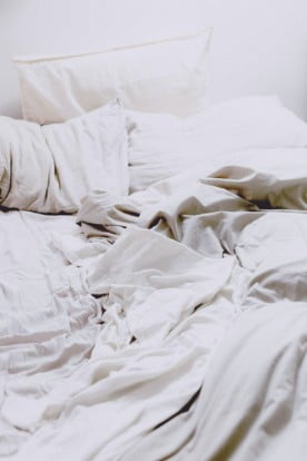 An untidy bed with white sheets and pillows.